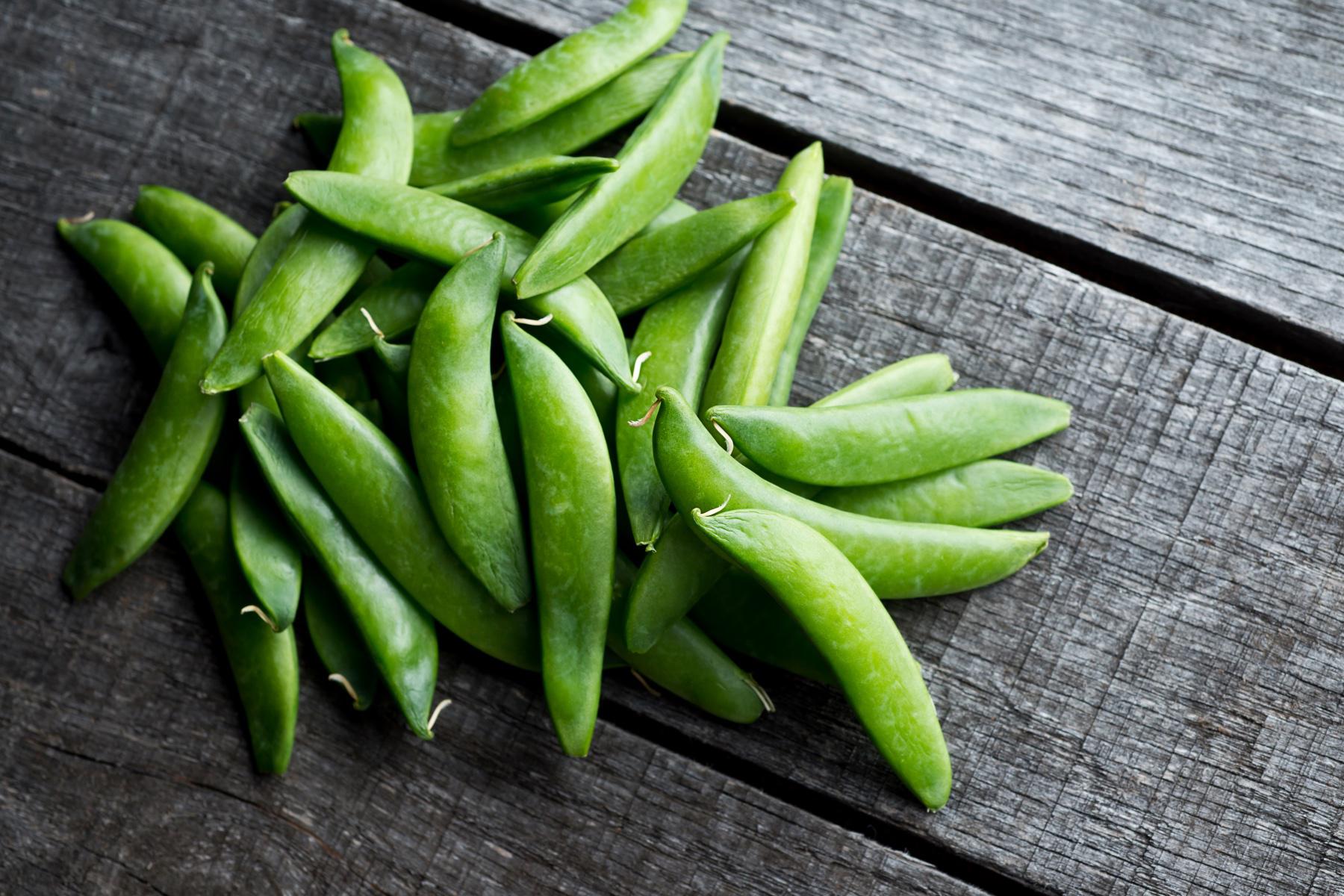 Pile of raw snap peas on dark wooden table.