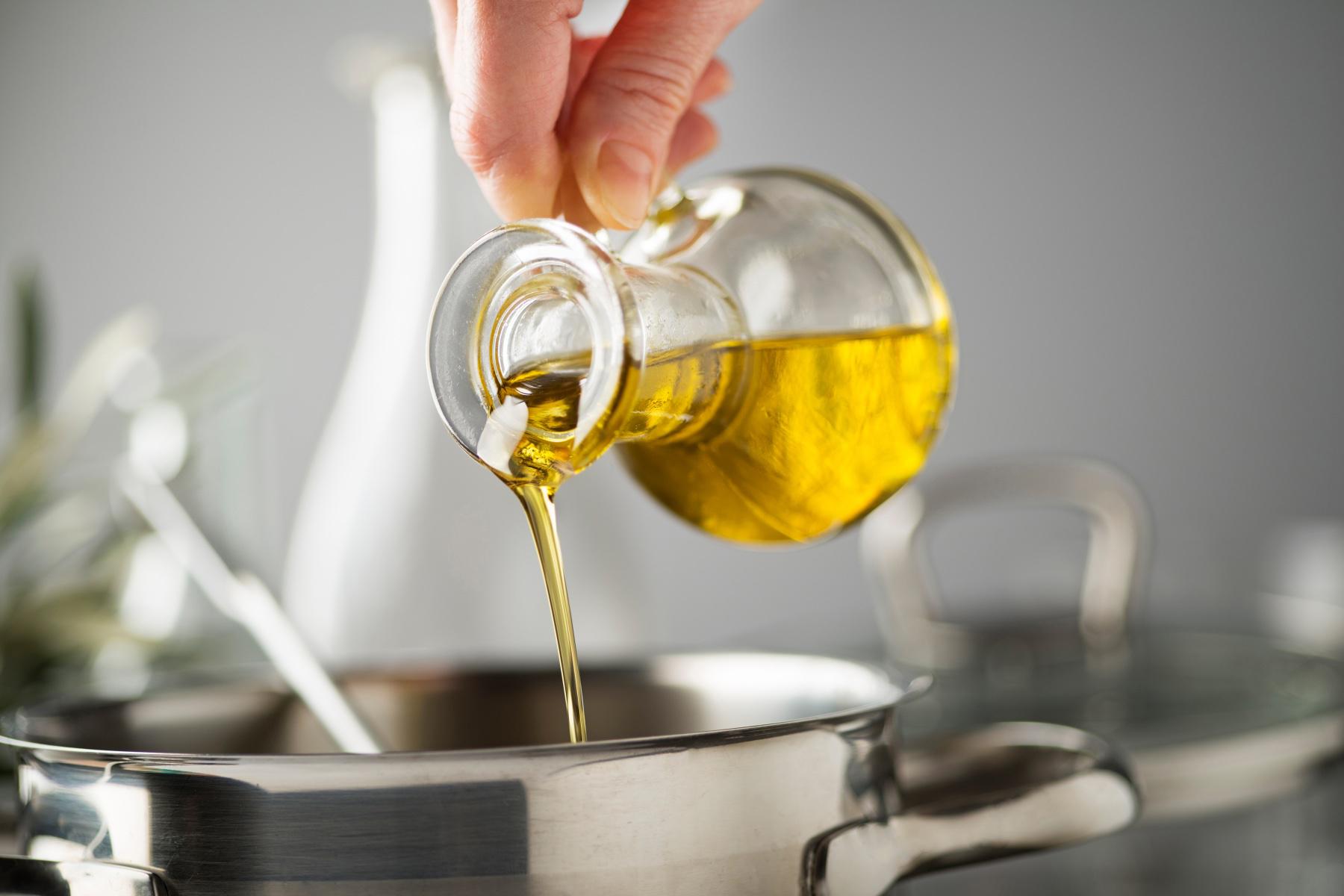 close-up of hand pouring olive oil into metal pot