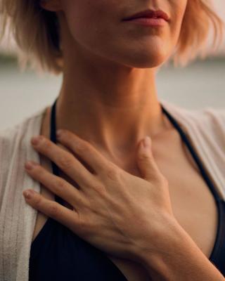 Image of woman with her hand resting on her chest wearing a black halter top with beige cardigan